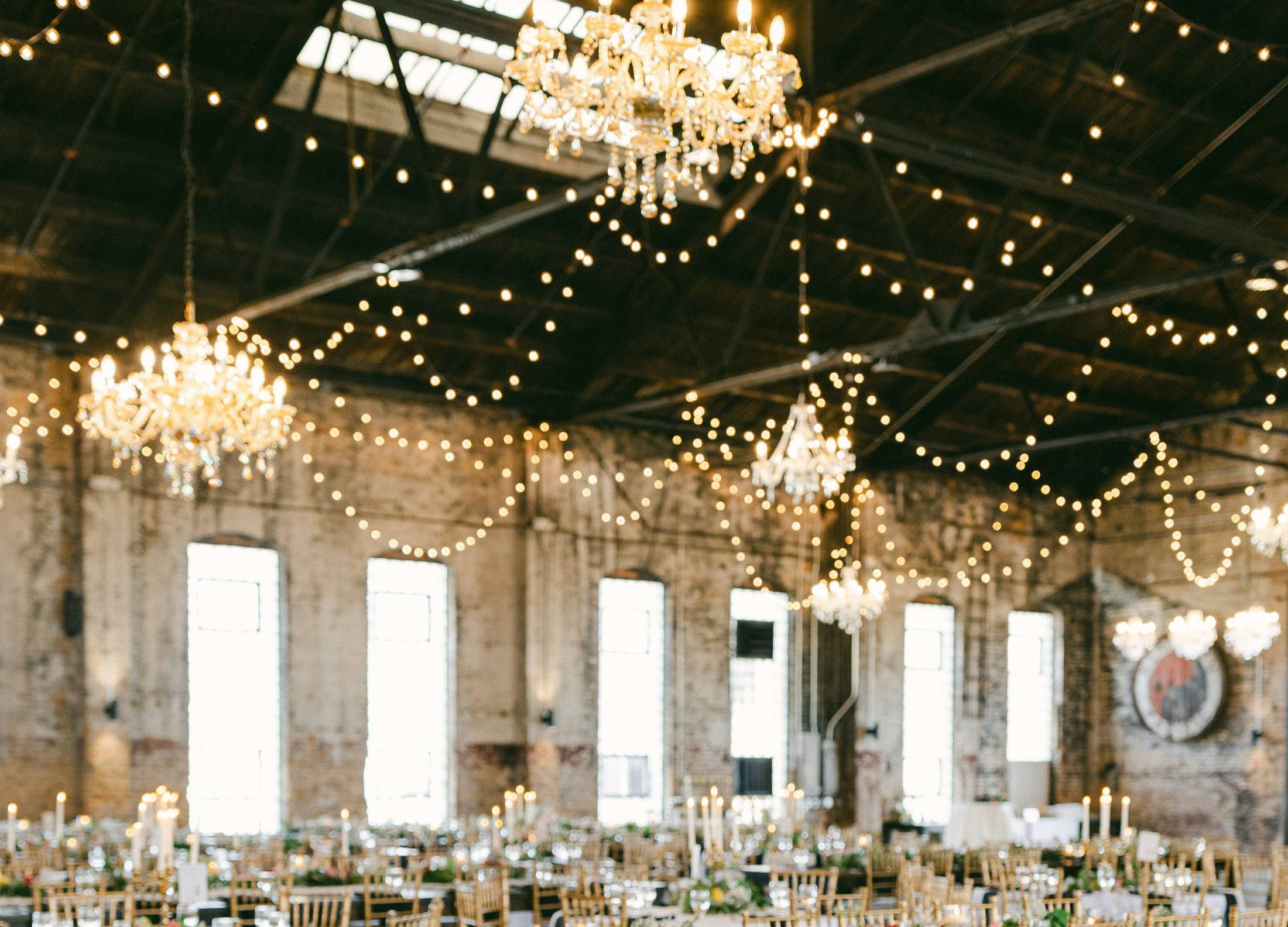 Wedding reception hall with chandeliers, string lights and long dinner tables