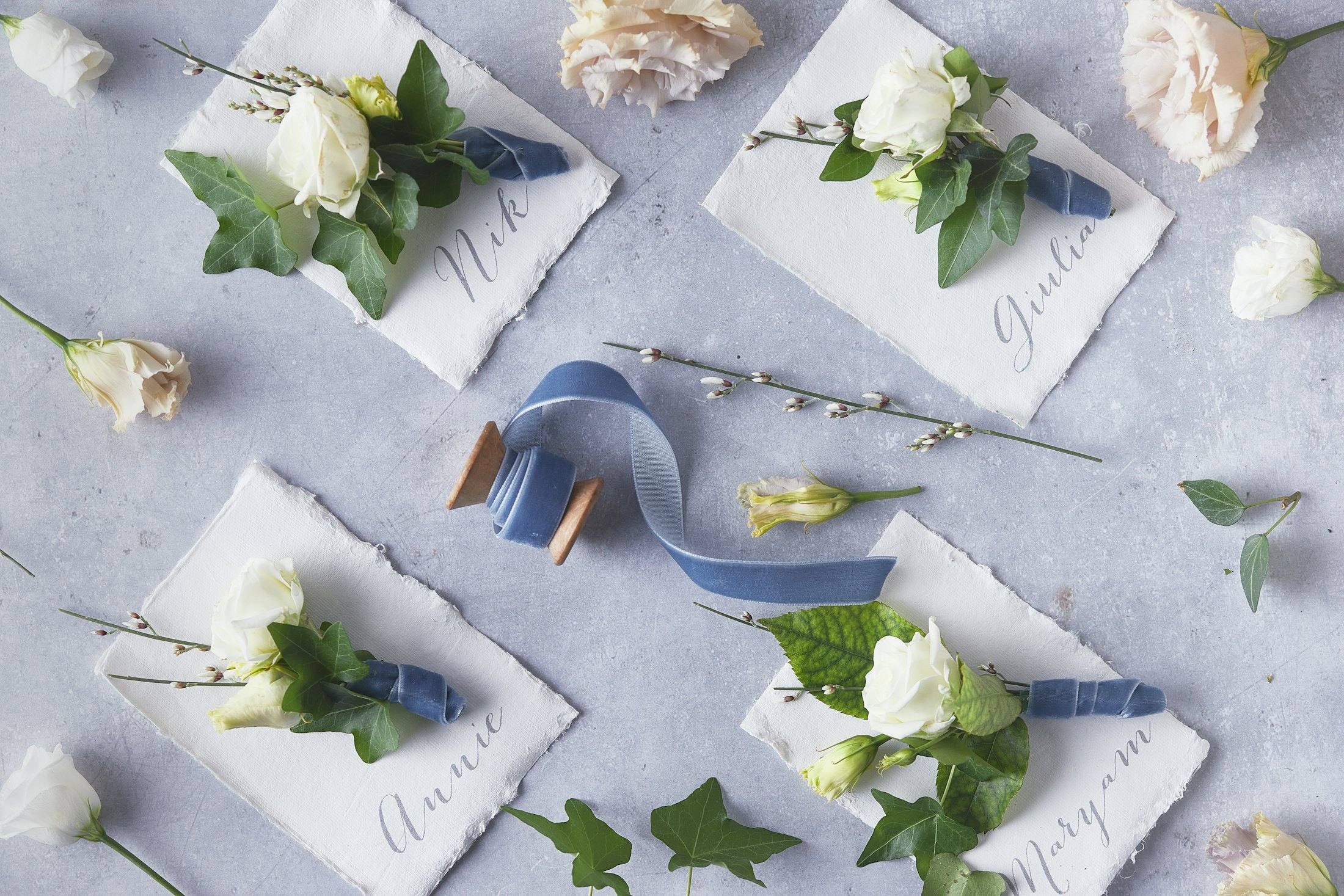 Hand-lettered place cards with white roses and dusty-blue ribbon